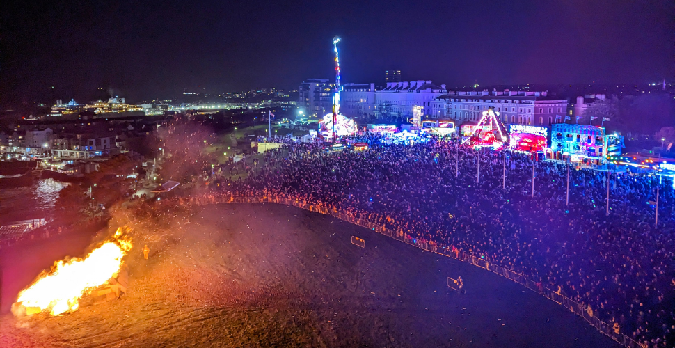 Bonfire Night on Plymouth Hoe. A bonfire on the left of the image as ccrowds of people watch on on the right